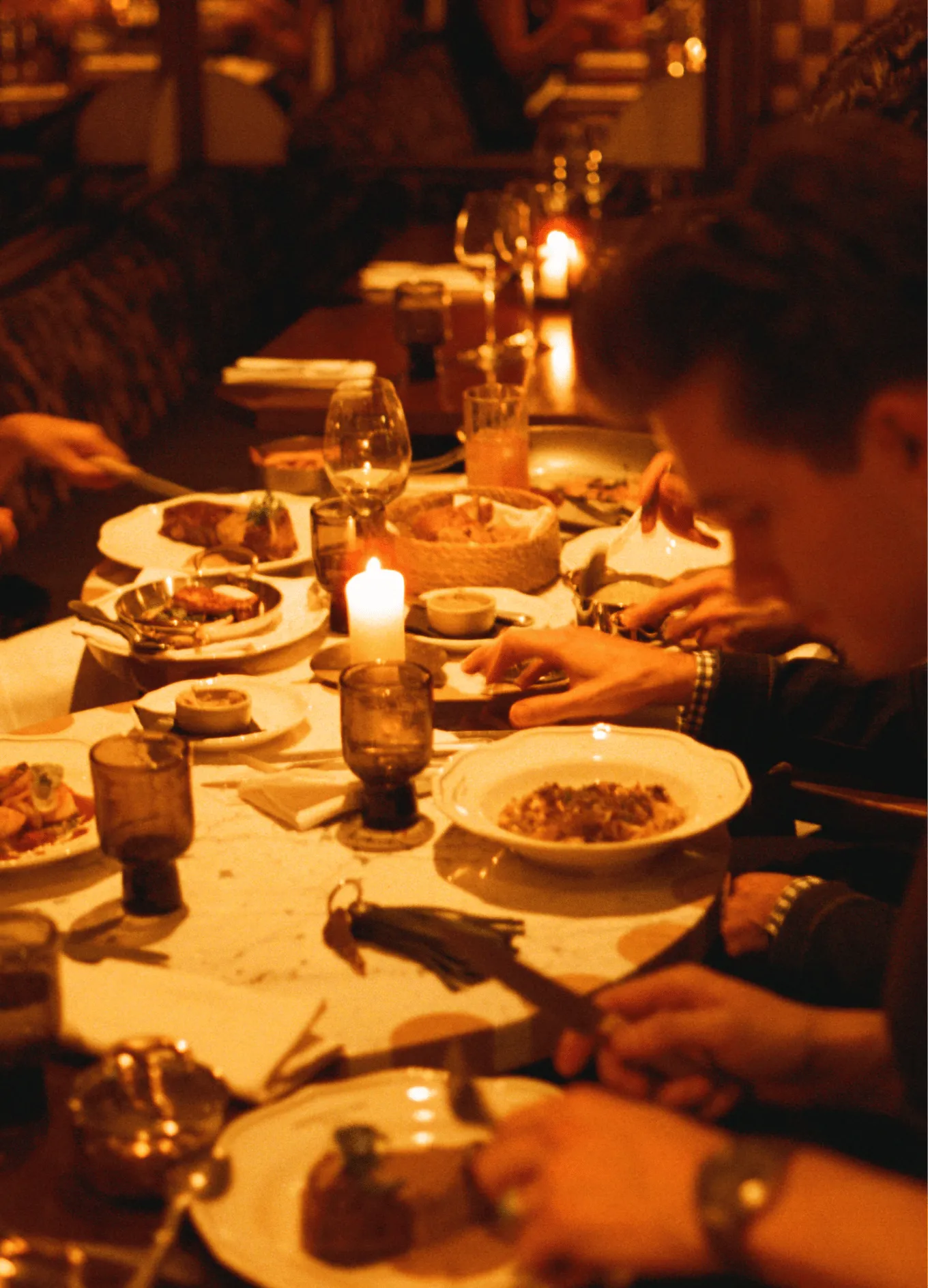 Candlelit dinner table with several people eating various dishes in a warm, cozy restaurant setting.