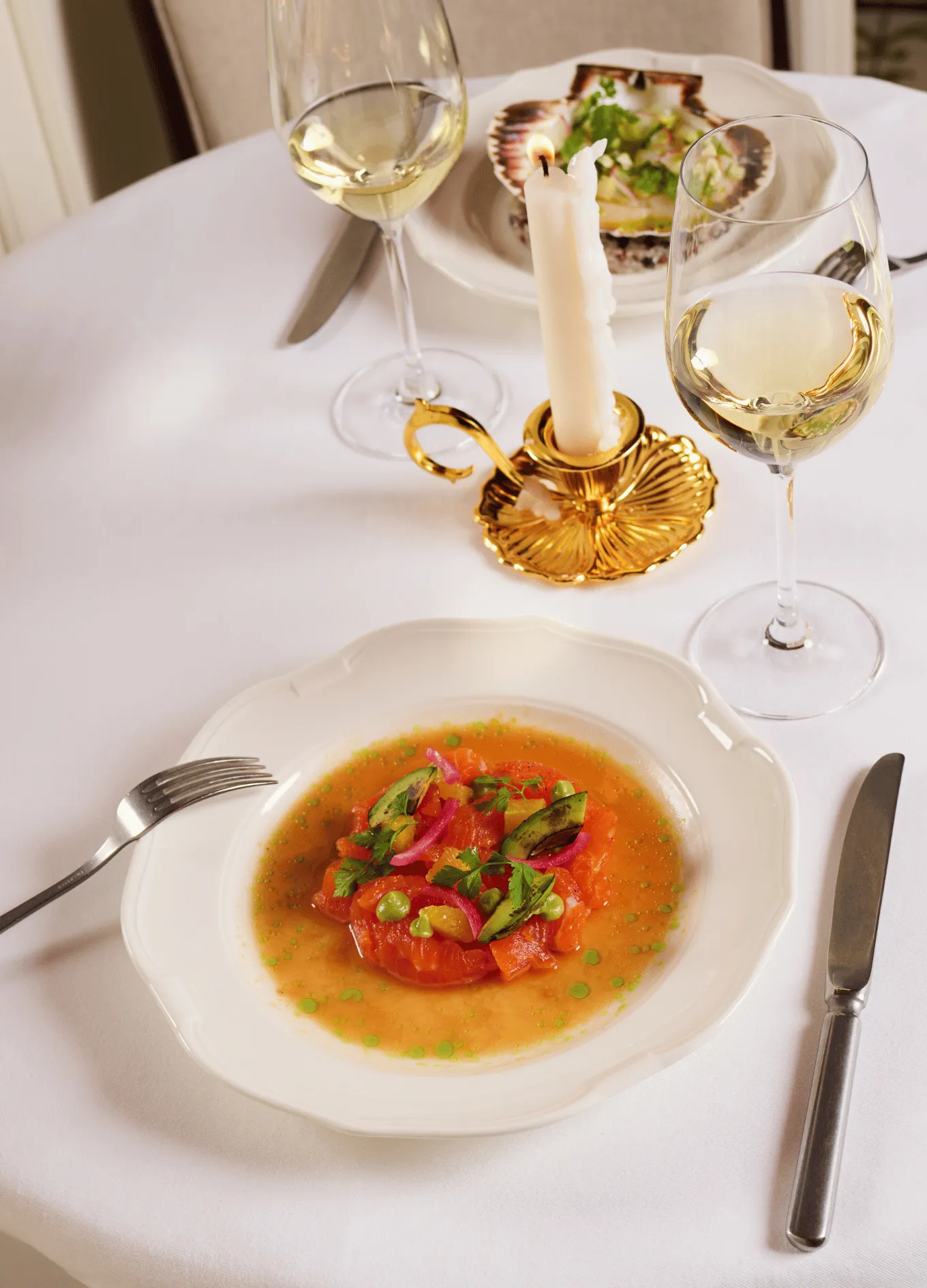Gourmet plate with colorful vegetable dish and green sauce, set on a white tablecloth with a lit candle and two glasses of white wine.