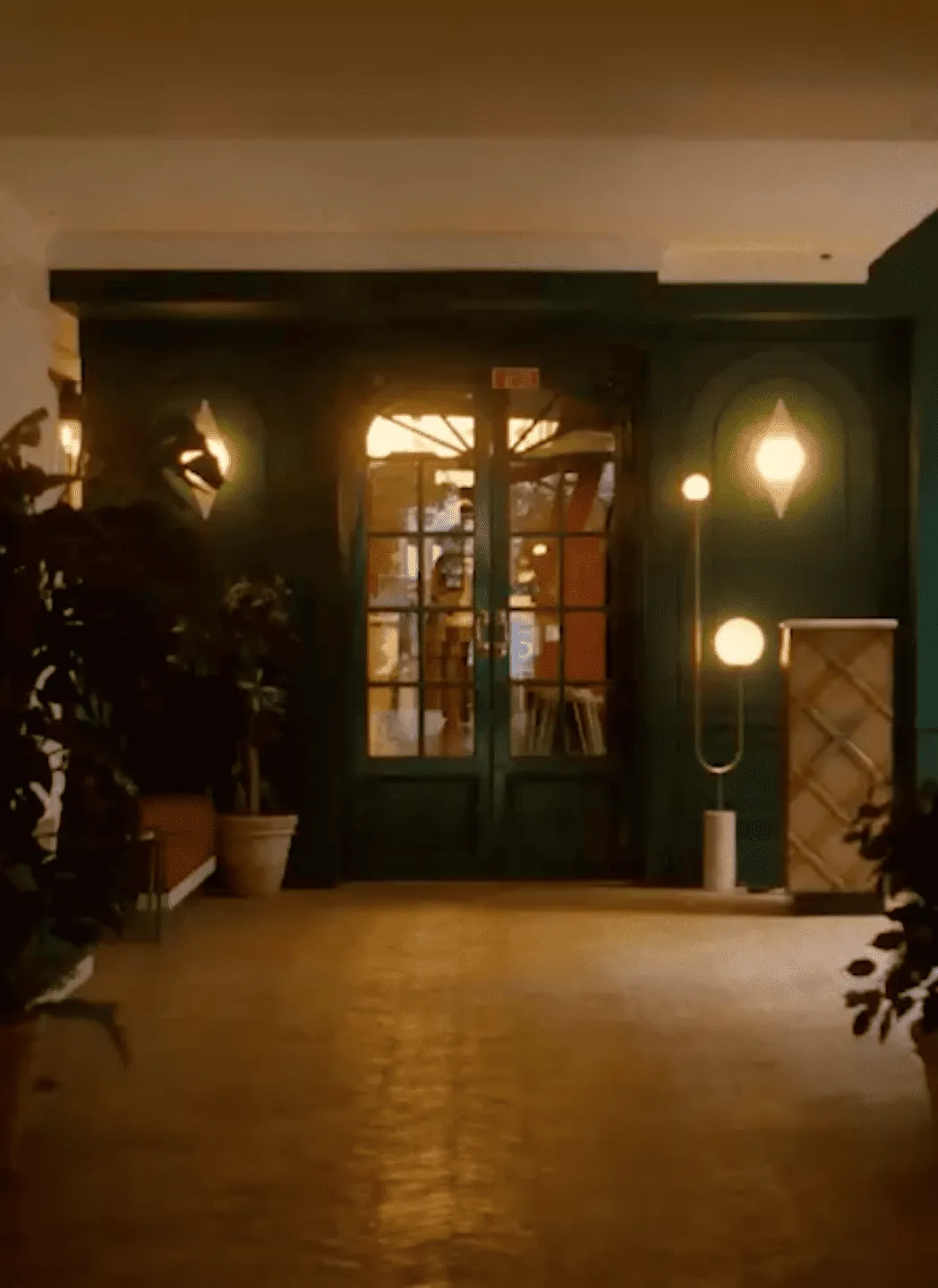 Chambre confortable faiblement éclairée avec des portes doubles en verre, des plantes en pot et des lampes murales et de sol modernes.