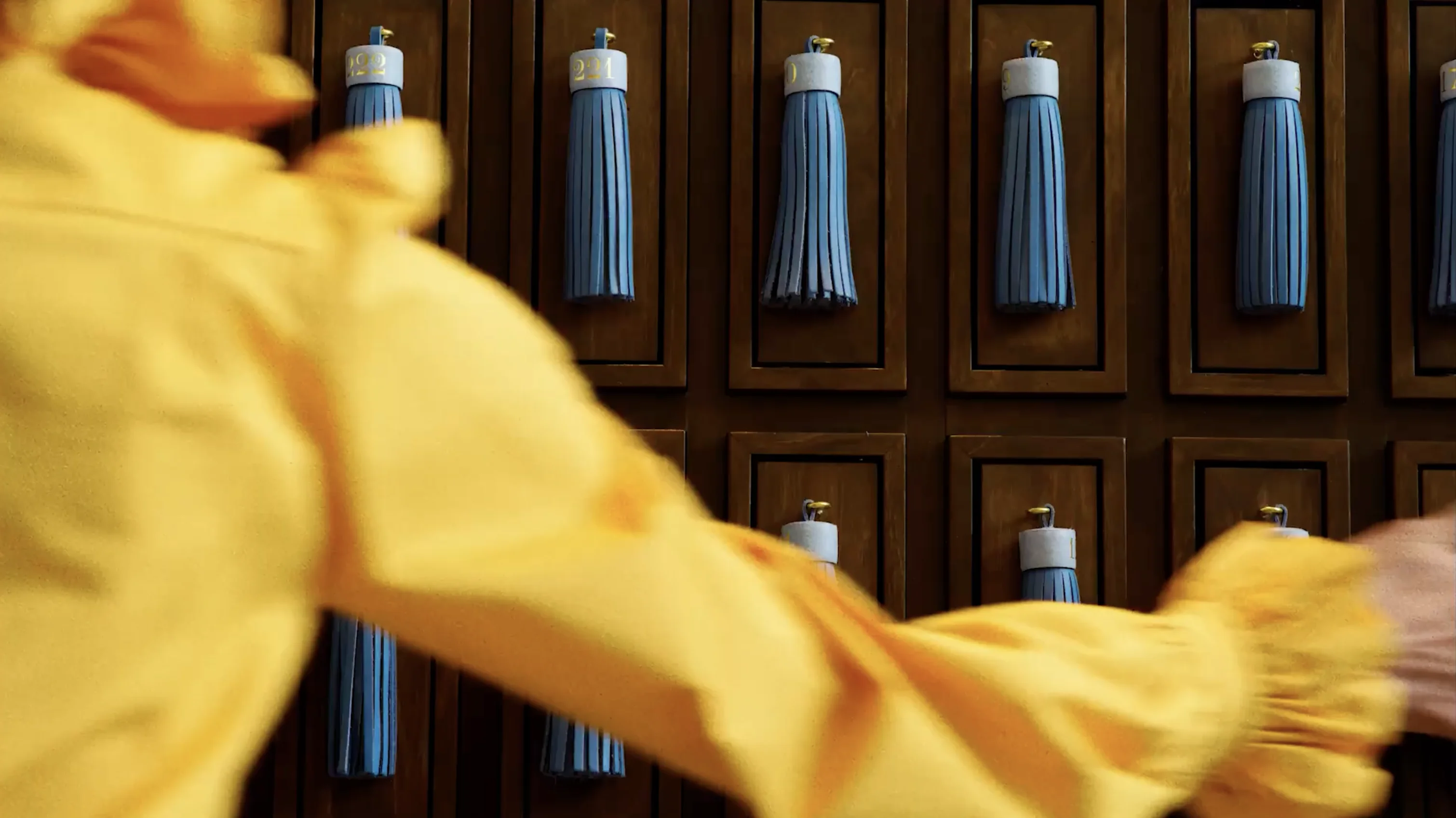 Person in yellow sleeve reaching toward wooden lockers with blue tassel keychains.