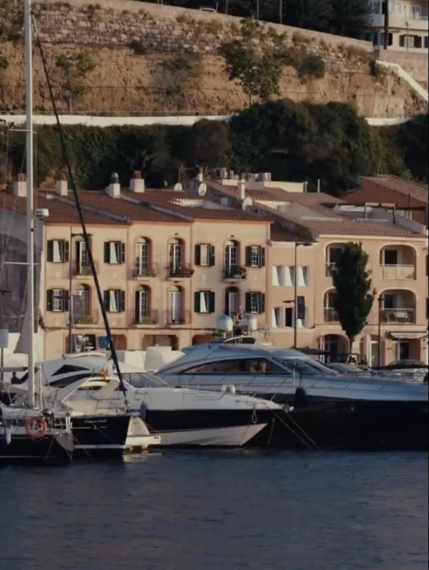 Motorboats docked on calm water in front of Mediterranean-style buildings with green shutters and terracotta roofs.