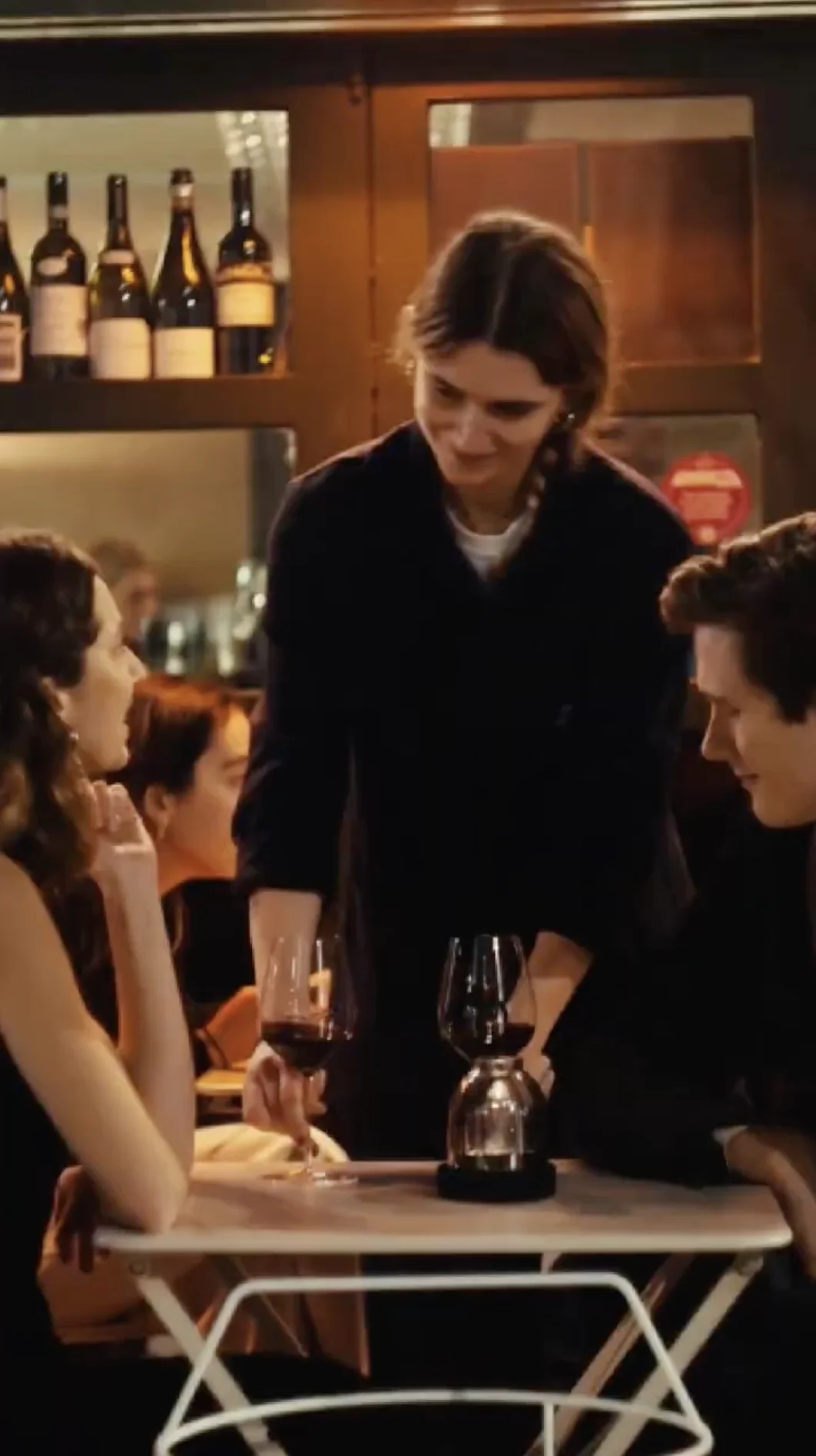 A waitress serving wine to a couple seated at a small table in a cozy restaurant bar.