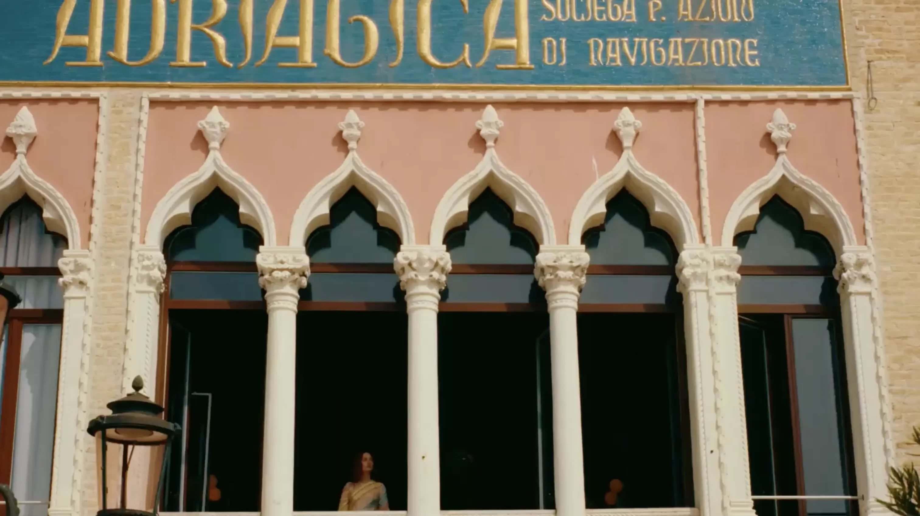 Balcony with Venetian Gothic arches and columns beneath a sign reading 'Adriatica Società P. Azioni di Navigazione'.