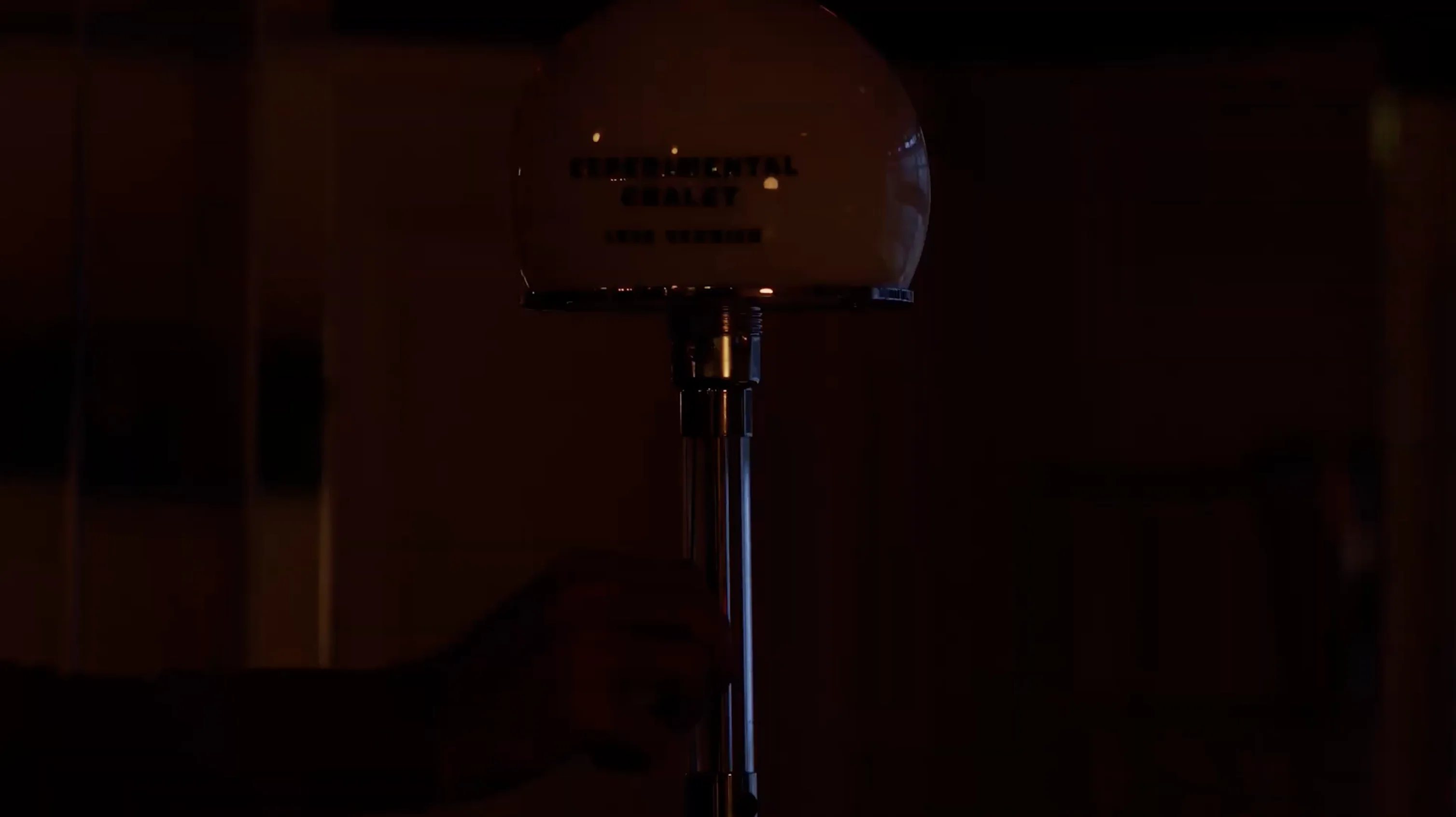 A dark room with a hand adjusting a metal pole supporting a spherical light fixture.