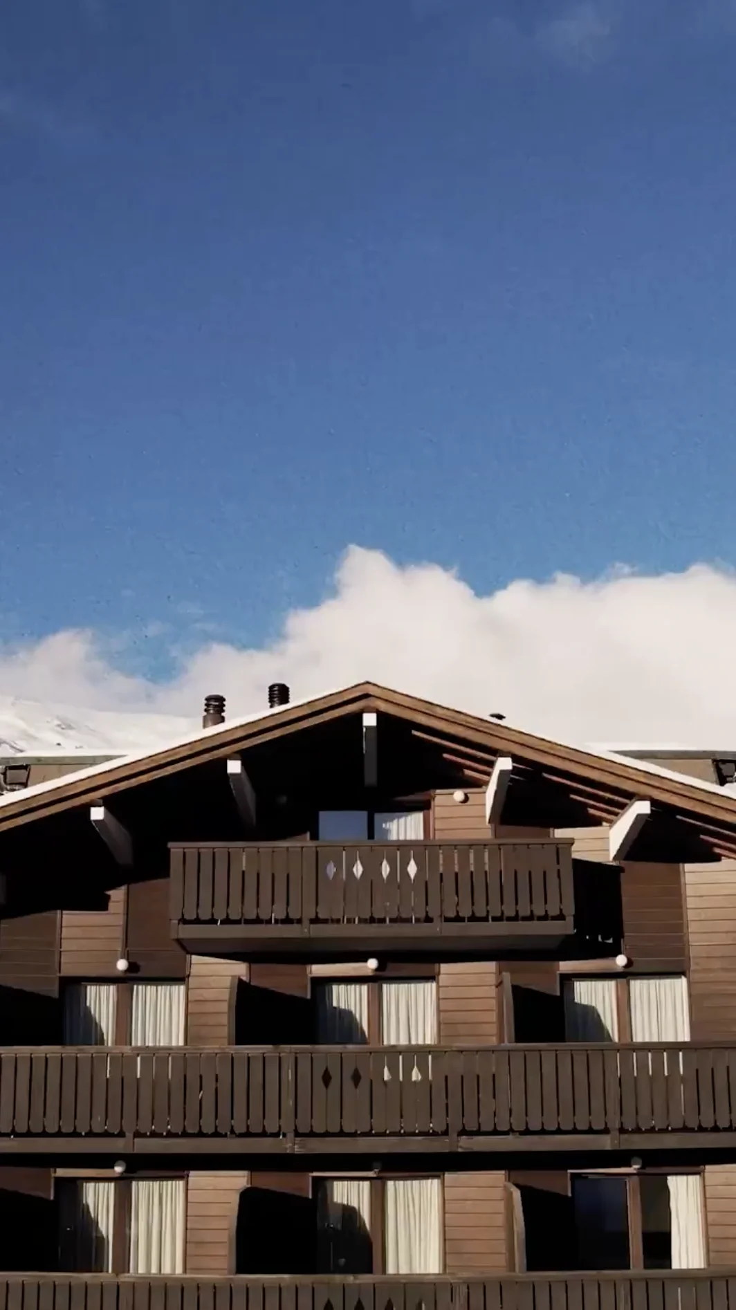 Wooden chalet with balconies under a clear blue sky with white clouds.