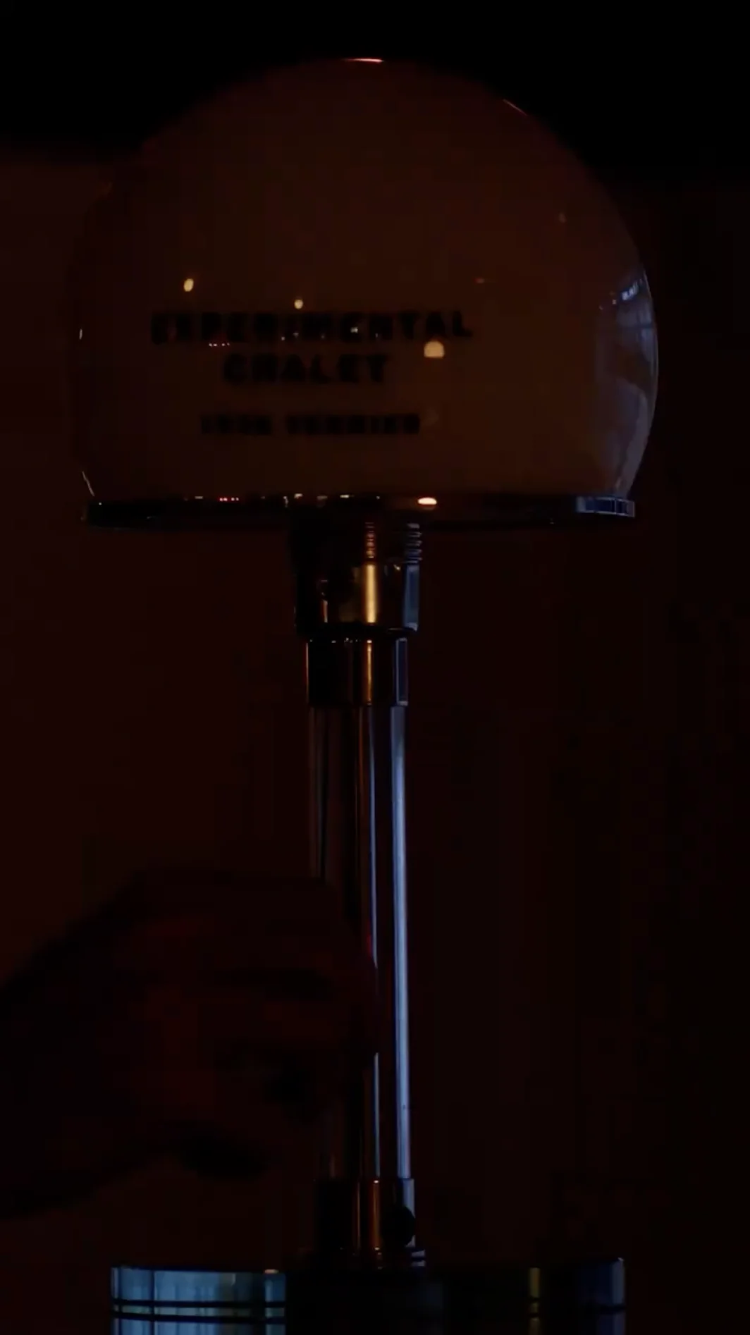 Hand adjusting a vintage-style microphone stand with an illuminated round head in a dark setting.