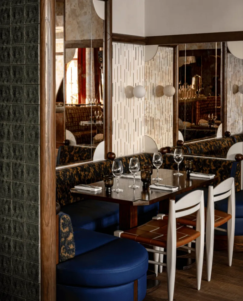 Cozy restaurant table set with wine glasses, napkins, and cushioned seating with decorative mirrors on the wall.