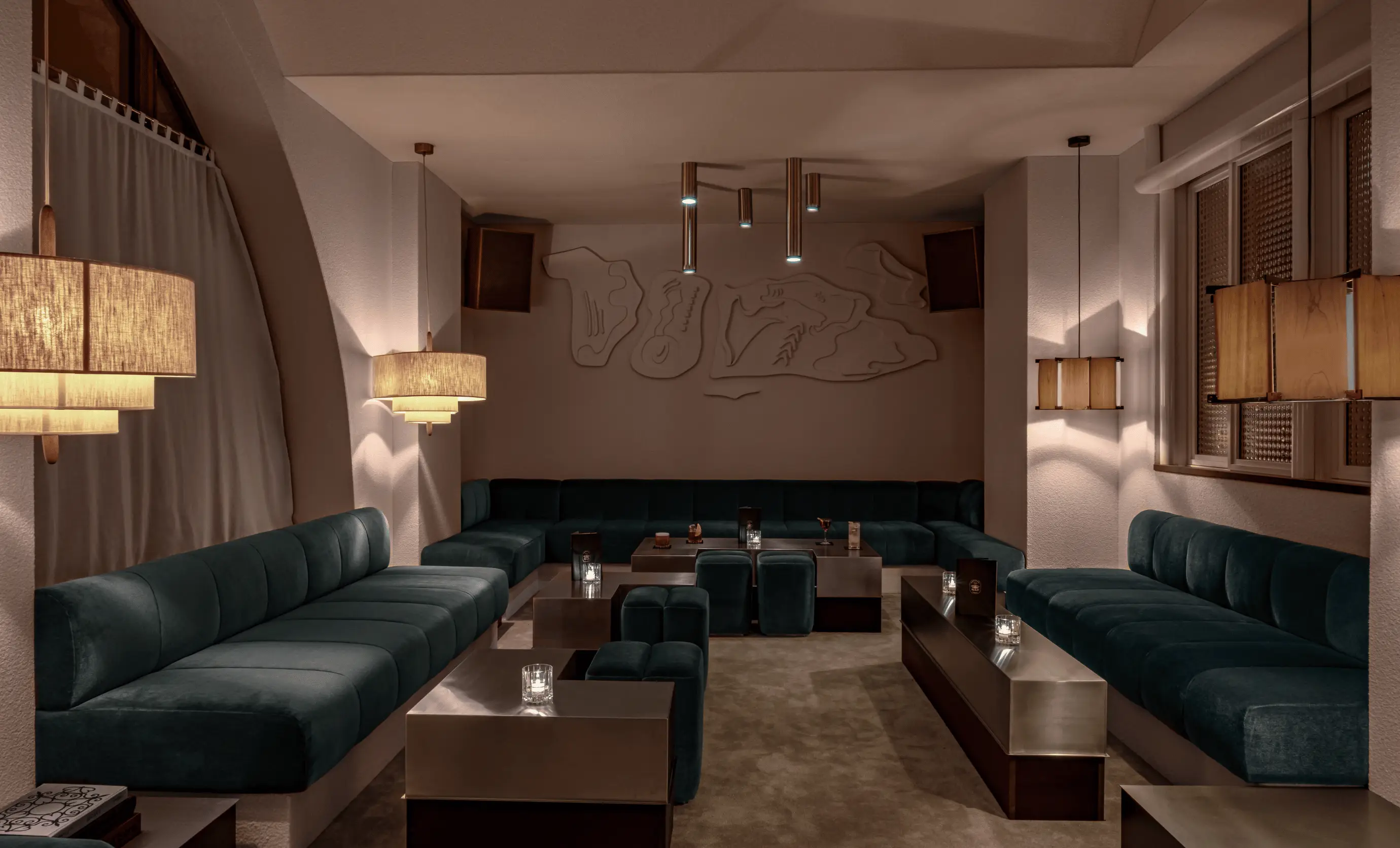 Modern lounge area with dark teal sofas, metallic coffee tables, and warm pendant lighting.
