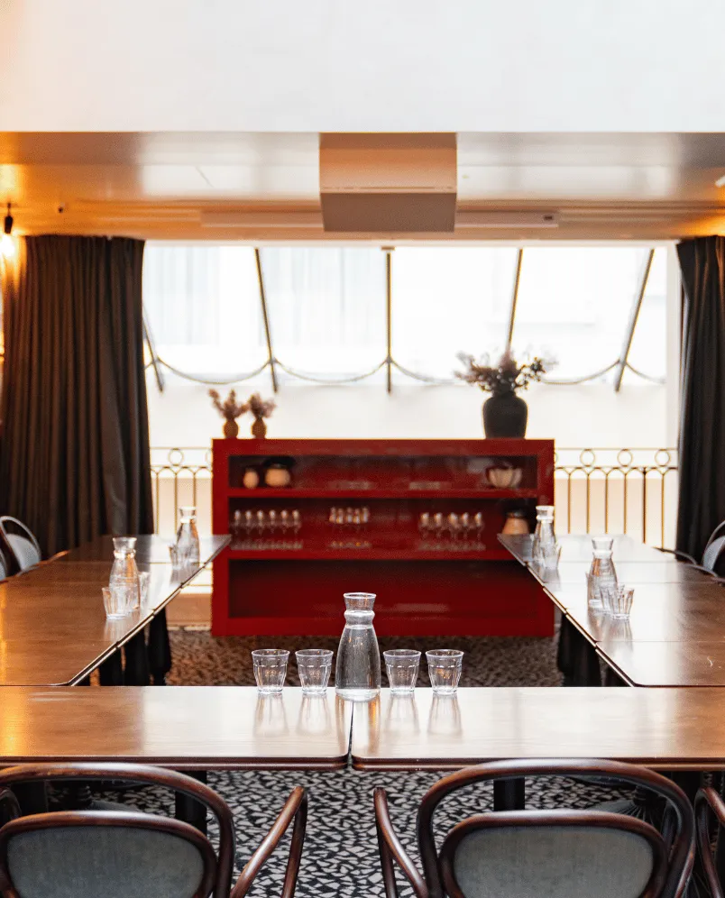 U-shaped conference table with water pitchers and glasses in a bright meeting room with a red cabinet and large windows.