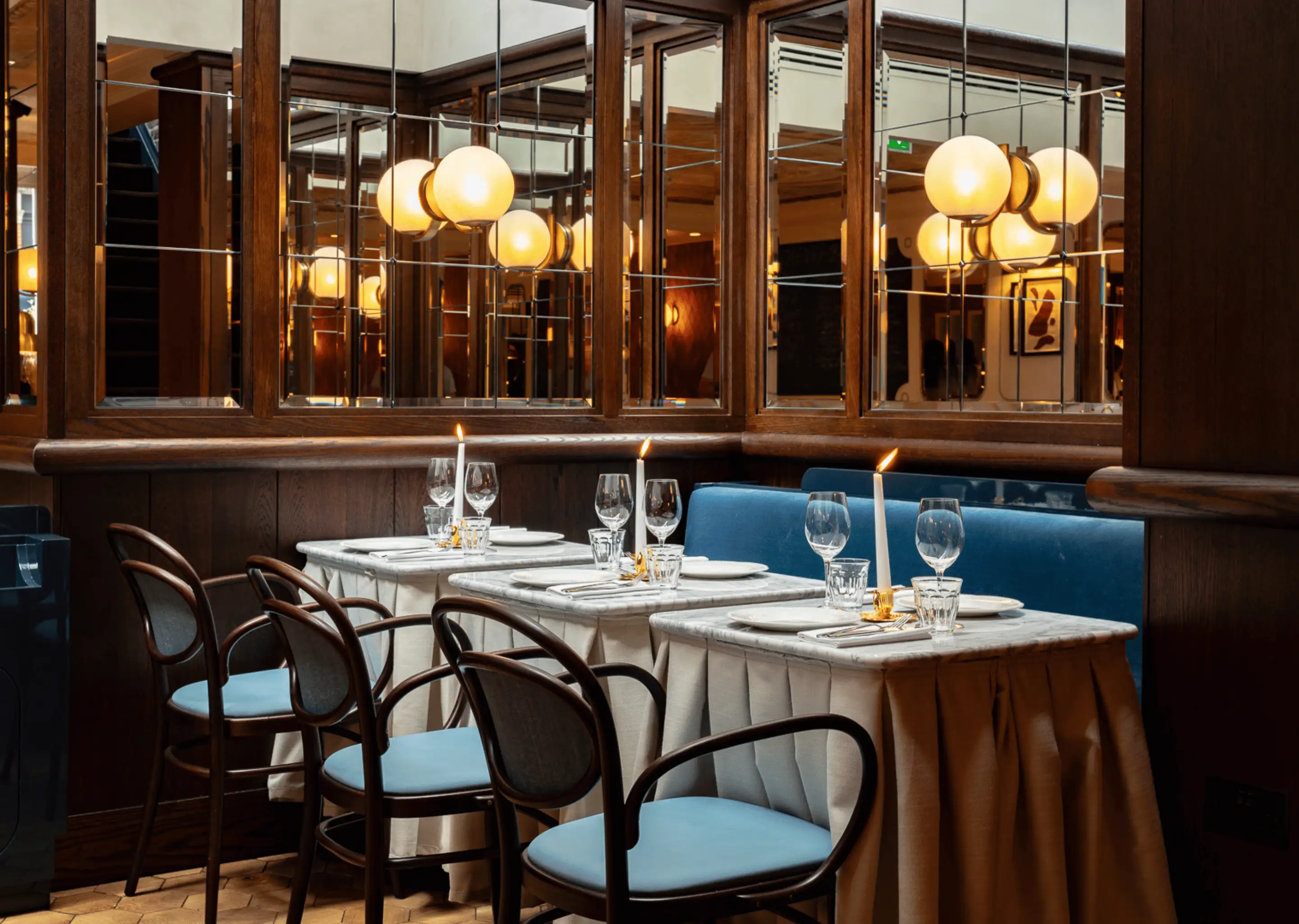 Elegant restaurant corner with marble-topped tables set with wine glasses, lit candles, and blue cushioned chairs.
