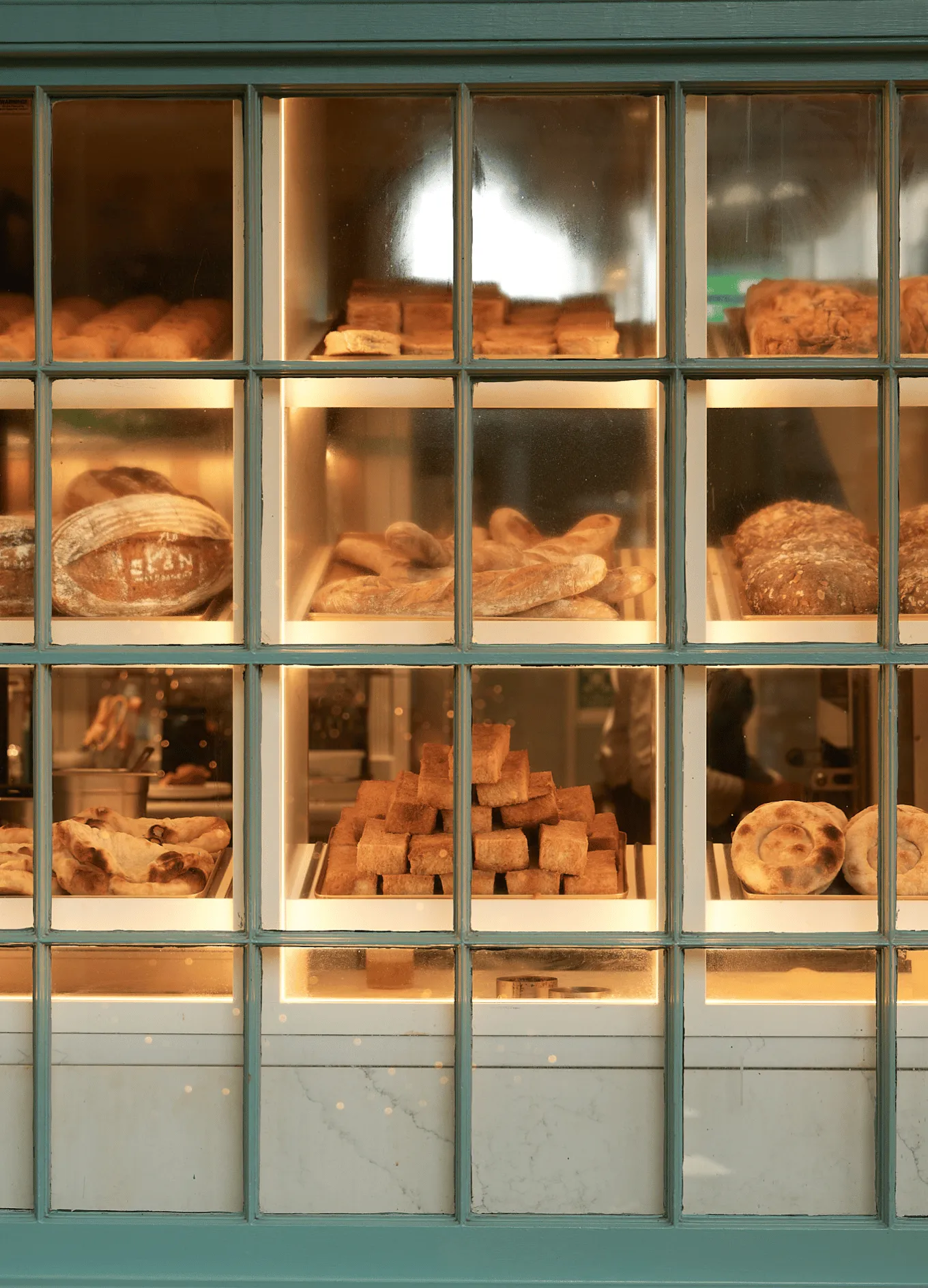 Display window of a bakery showcasing various kinds of bread loaves, rolls, and baked goods on shelves.