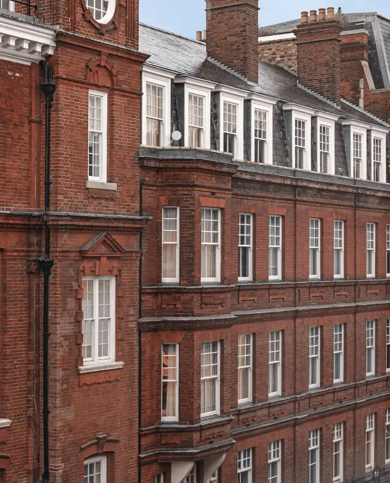 Facade of a red brick building with multiple white-framed windows, a slate roof, and prominent chimneys.