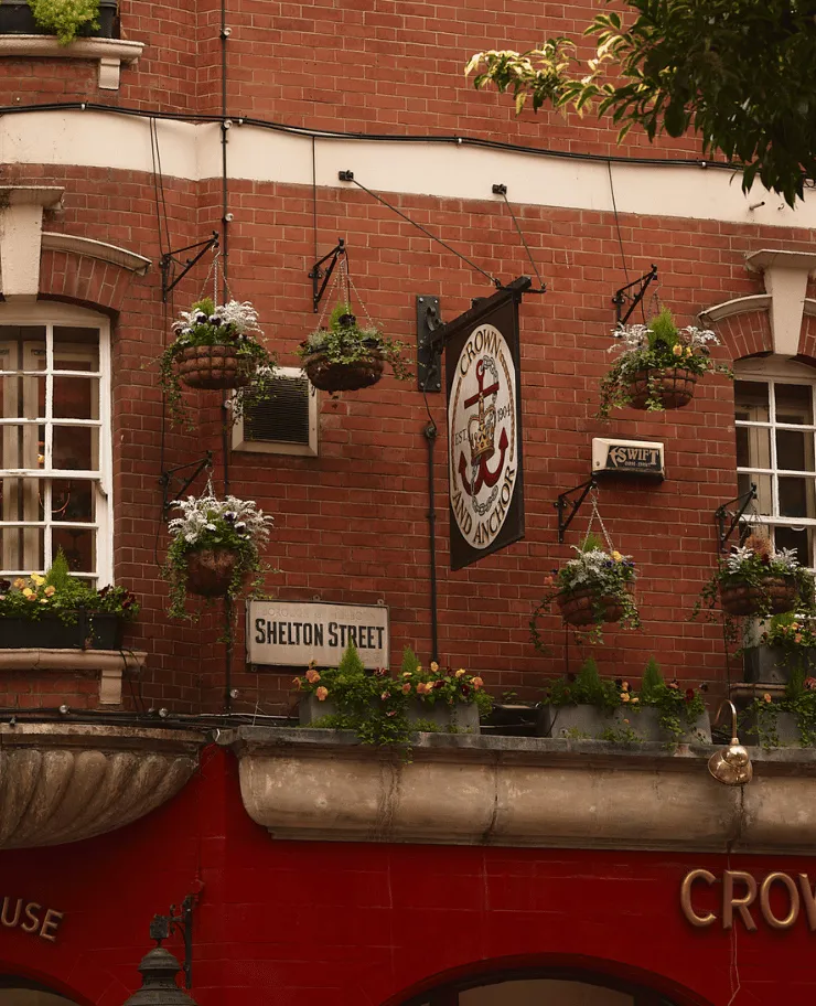 Brick building facade with hanging flower baskets, Shelton Street sign, and a Crown and Anchor pub sign with anchor emblem.
