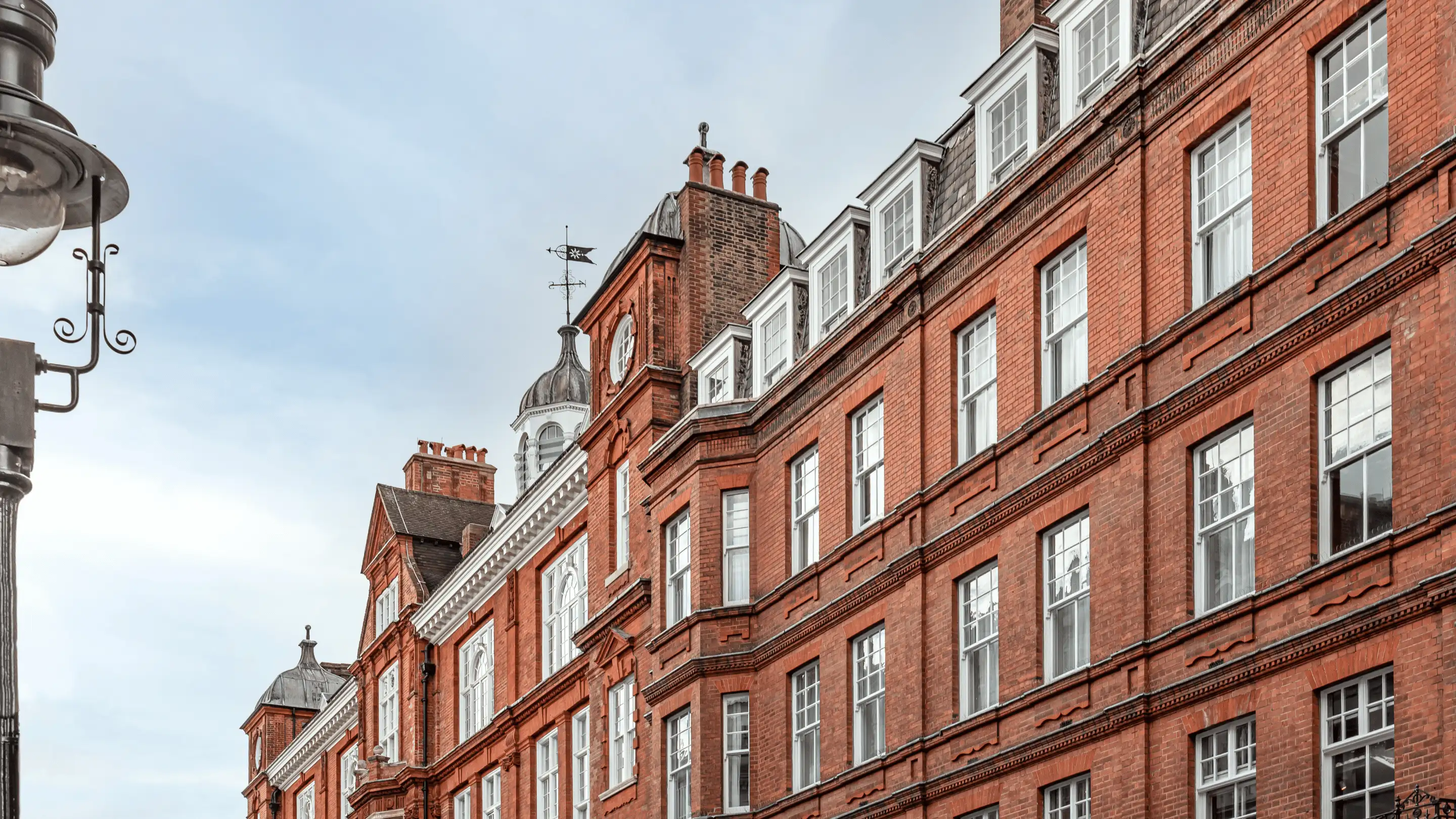 Historic red brick building with large windows and ornate roof structures under a cloudy sky.