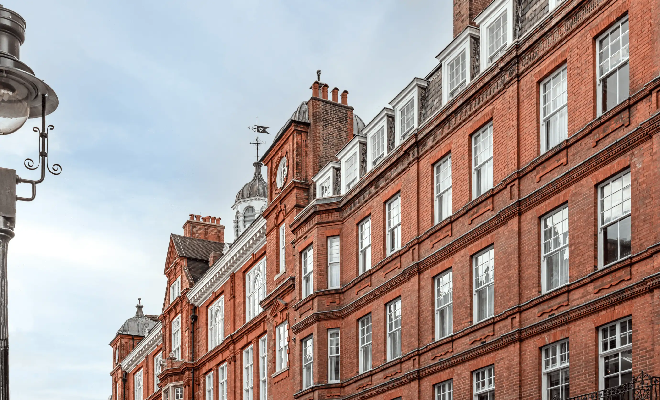 Red brick historic building with multiple white-framed windows and a clock tower under a cloudy sky.