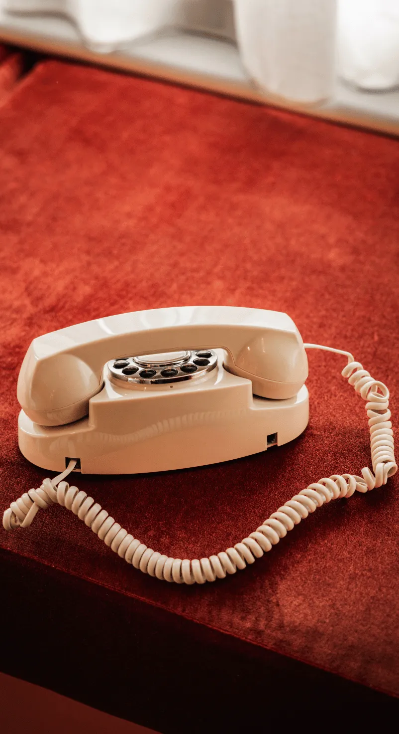 Cream-colored rotary dial telephone with coiled cord on a red velvet surface.