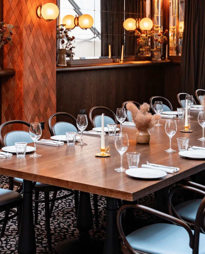 Elegant restaurant table set with wine glasses, water glasses, white plates, napkins, candles, and a small vase with dried flowers.