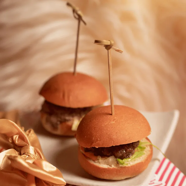 Two mini cheeseburgers with lettuce and sauce on a white rectangular plate, each held by a wooden skewer.