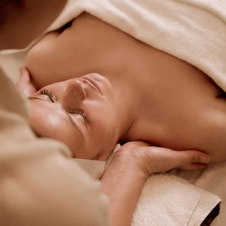 Relaxed woman receiving a shoulder massage wrapped in a white towel in a spa setting.