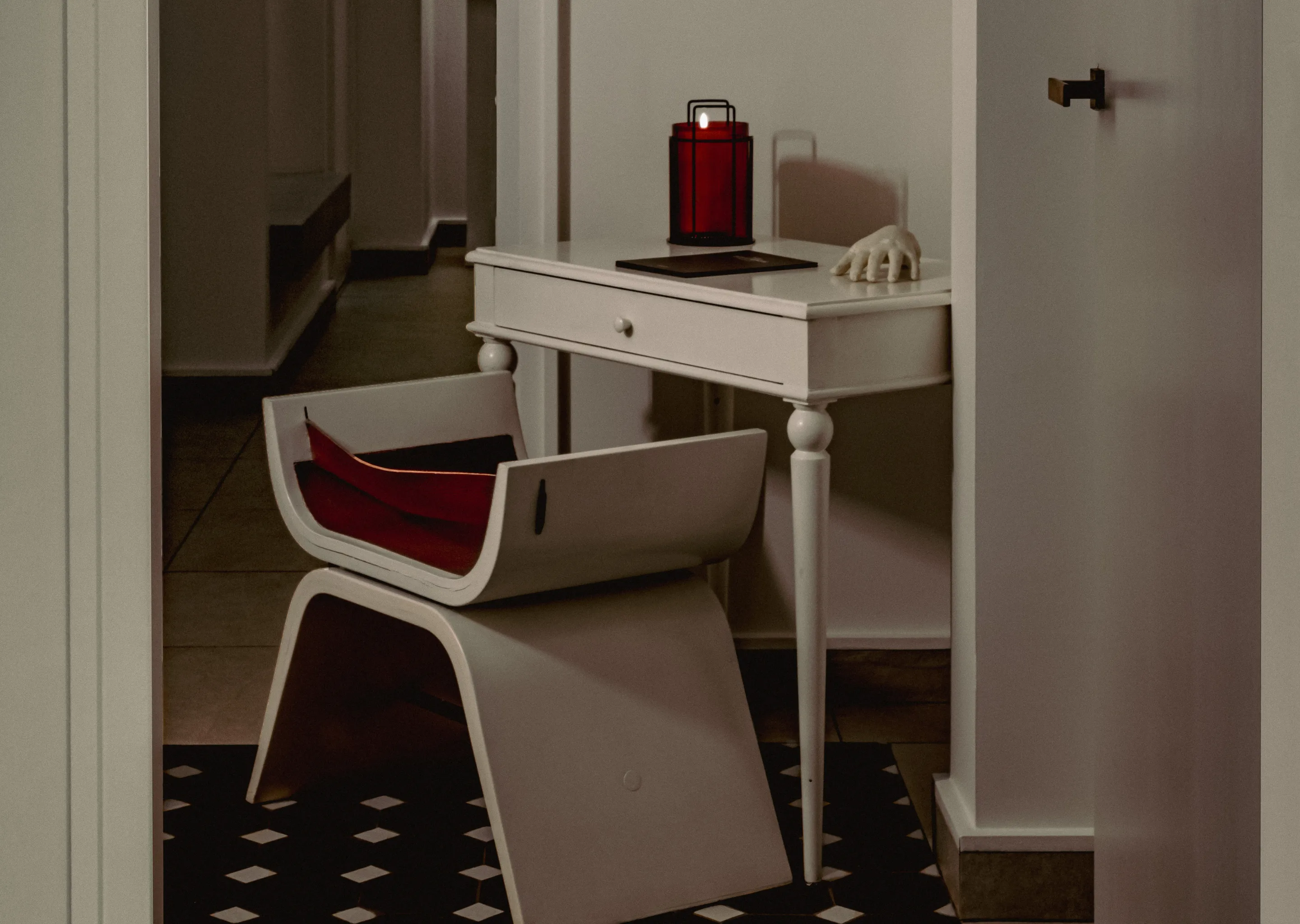 Modern white chair with red cushions next to a small white table holding a red lantern and a white decorative hand.