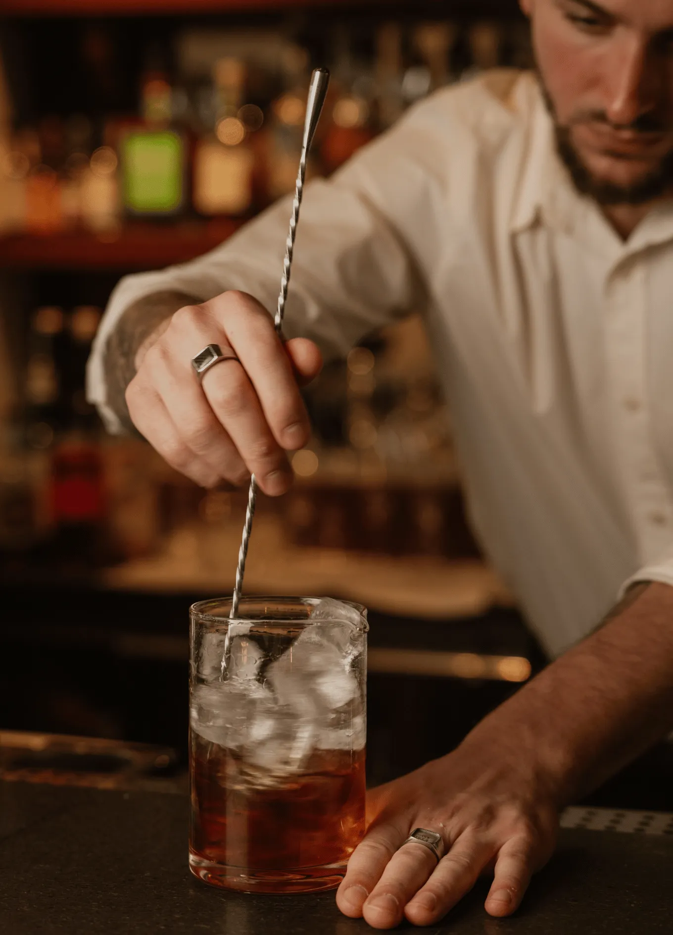 Bartender stirring a drink with ice in a mixing glass using a twisted bar spoon.