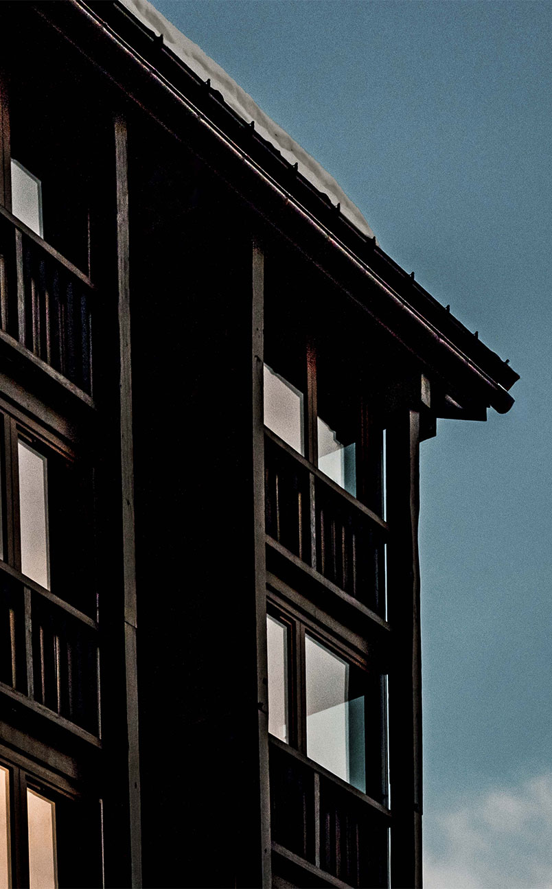 Close-up of dark wooden building corner with reflective windows against a clear blue sky.