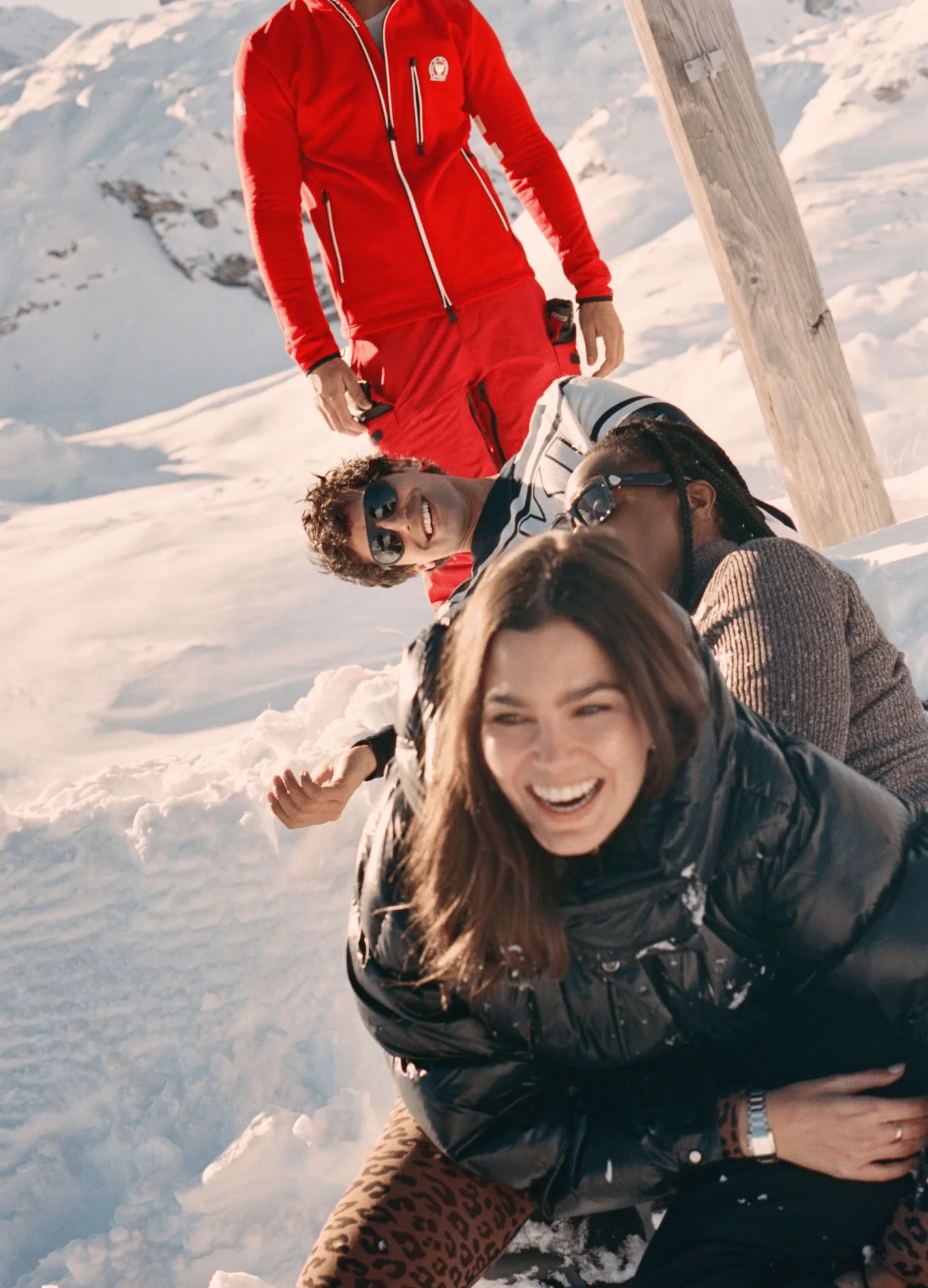 Group of friends smiling and relaxing on snow in a sunny mountain setting.