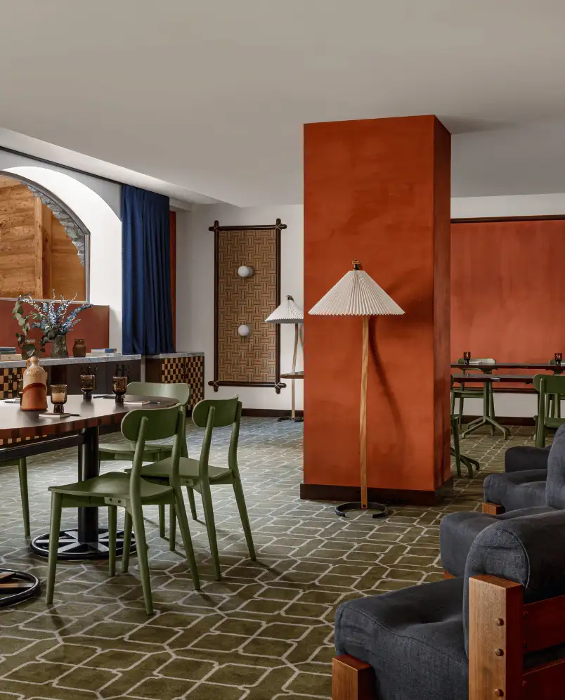 Indoor seating area with green chairs around tables, dark blue armchairs, and orange accent walls in a modern restaurant.