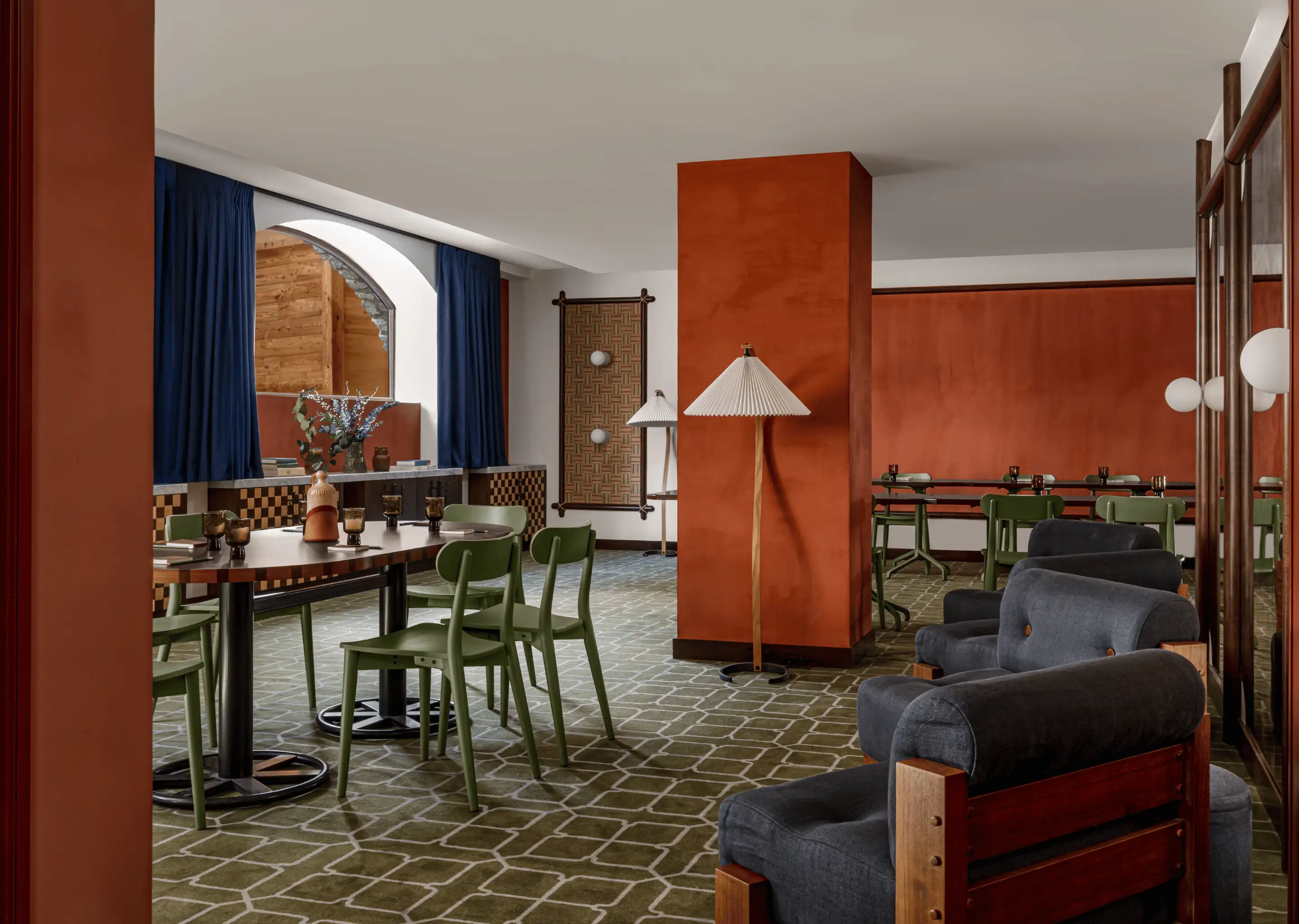 Modern restaurant interior with olive green chairs, dark wood tables, blue curtains, burnt orange walls, and cushioned armchairs.