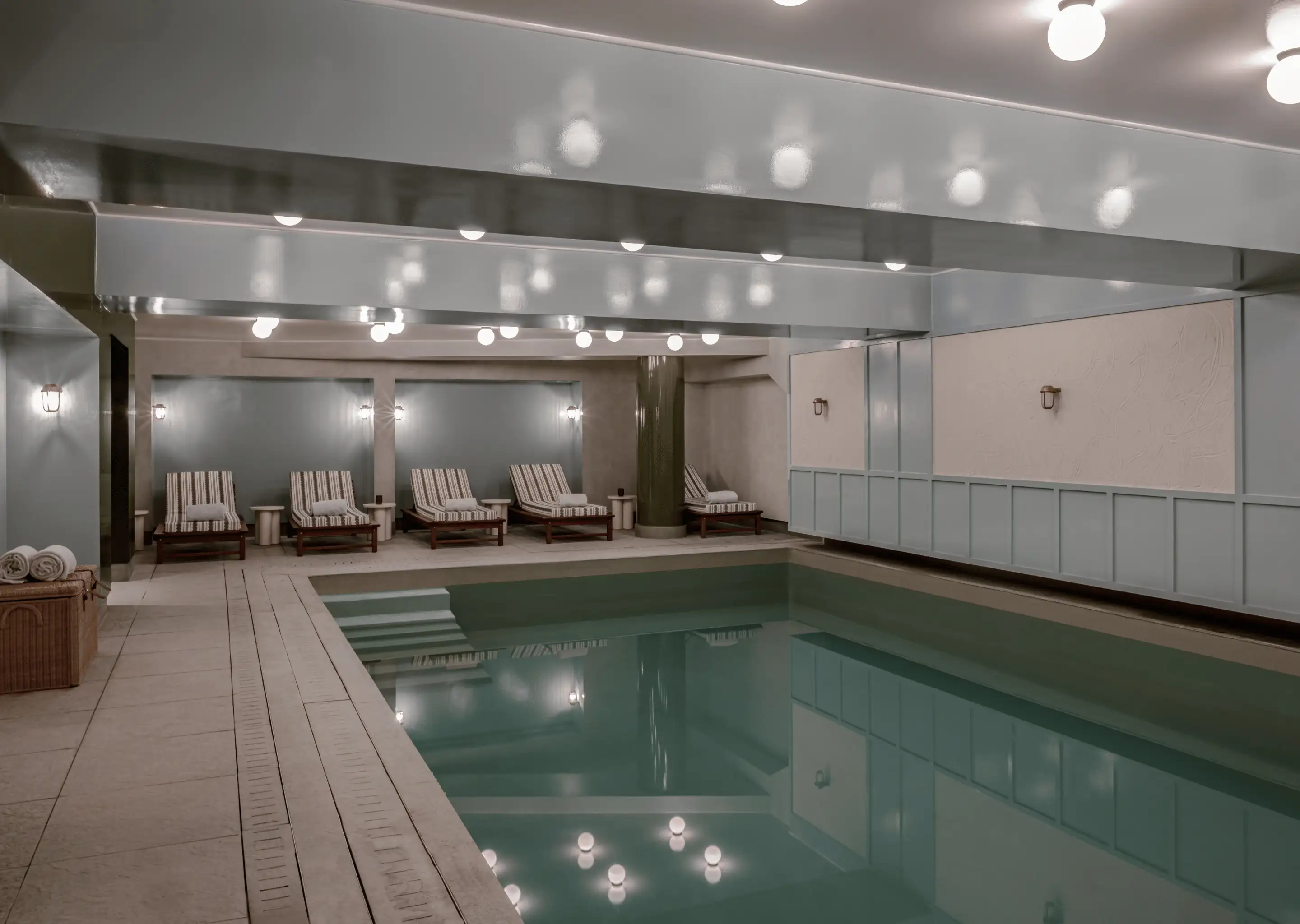 Indoor swimming pool with five striped lounge chairs and soft overhead lighting reflecting on the water.