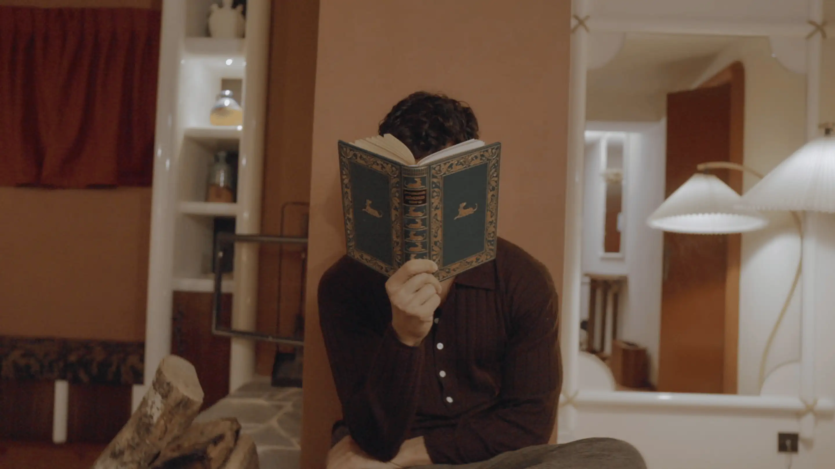 Man sitting indoors reading a decorative hardcover book that covers his face.