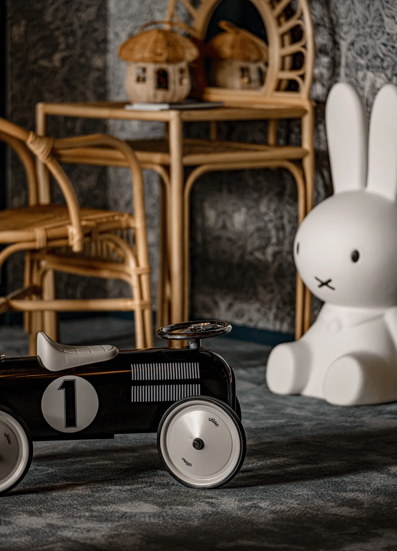 Black toy car with the number 1 next to a large white rabbit figurine in a room with wicker furniture.