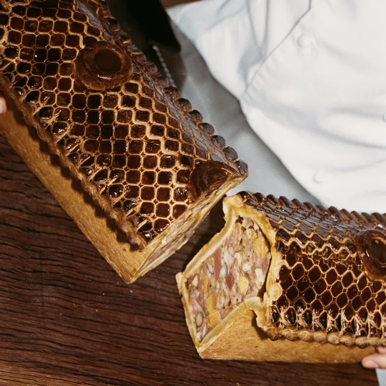 A pâté en croûte with a glossy, patterned crust, cut open to reveal a mixed meat filling with visible nuts.