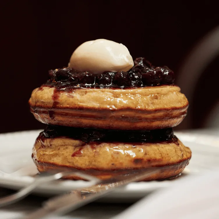 Stack of two golden-brown pancakes topped with blueberry compote and a dollop of butter on a white plate.