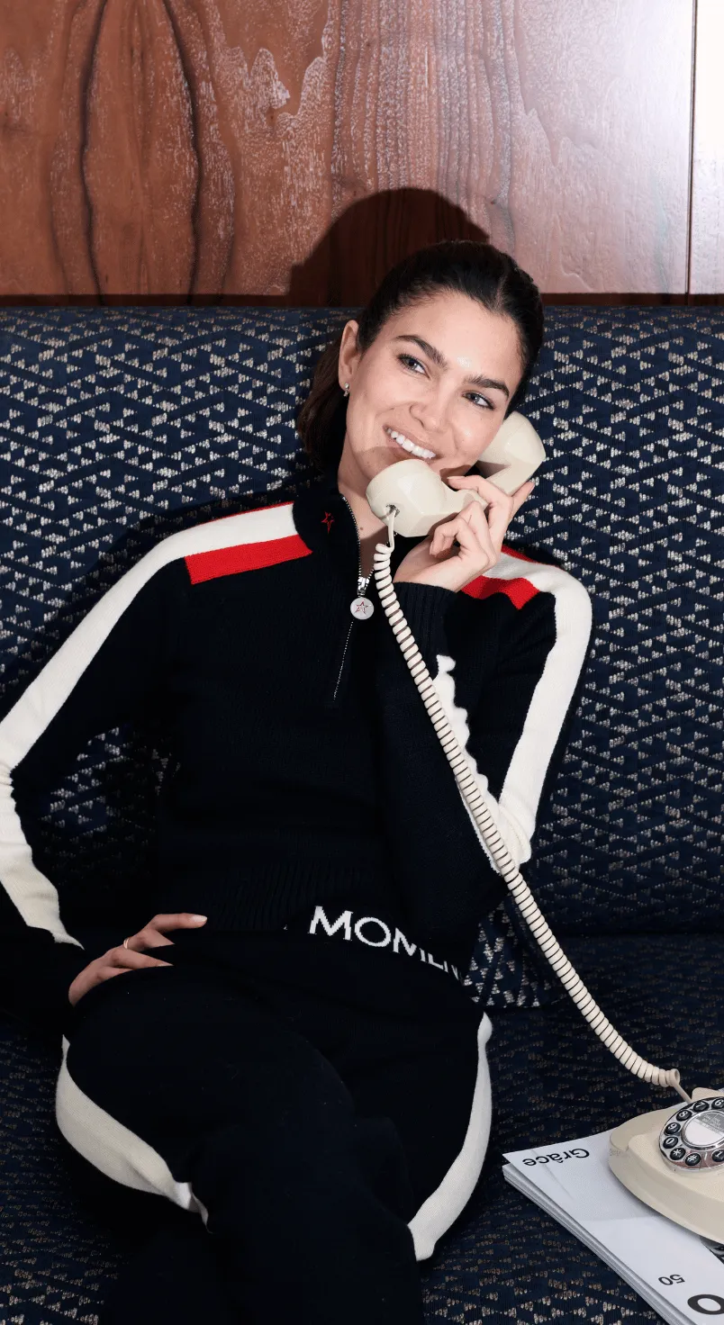 Smiling woman in black and white athletic wear sitting on patterned couch talking on a beige rotary phone.