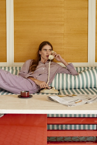 Woman in striped pajamas reclining on a striped couch while talking on a vintage rotary telephone.