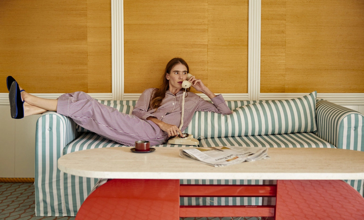 Person lounging on a striped sofa wearing purple striped pajamas and holding a beige rotary phone.