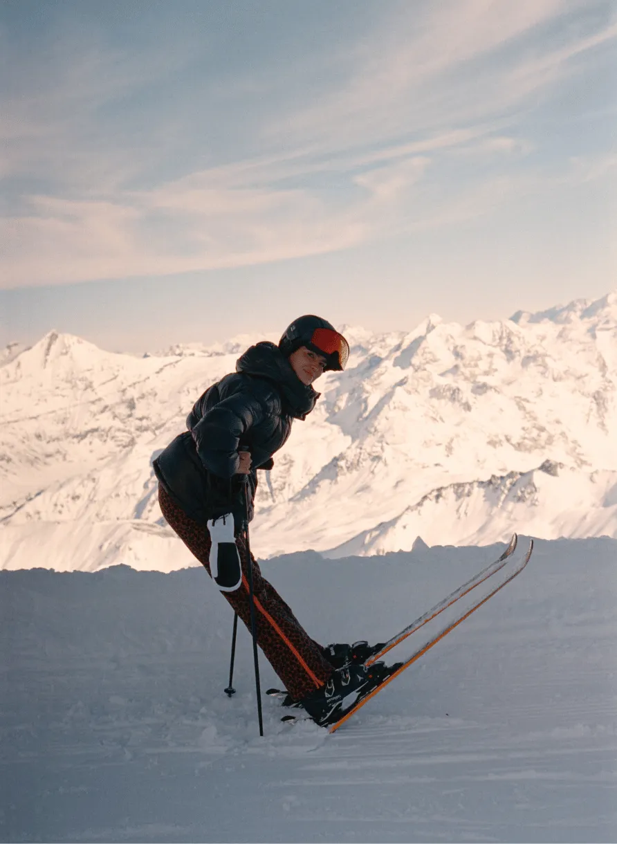 Person in a black ski jacket and helmet skiing on snow with snowy mountain range in the background.
