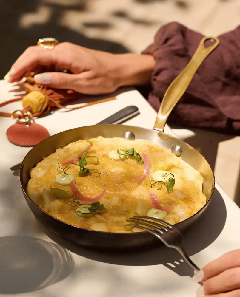 Frittata with herbs and pickled onions served in a small gold-handled skillet on a white table.