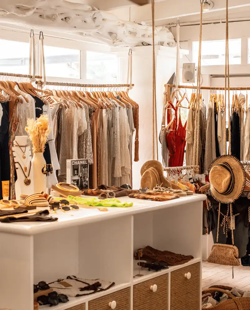 Bright boutique clothing store interior with hanging dresses, straw hats, accessories, and sunglasses on display.