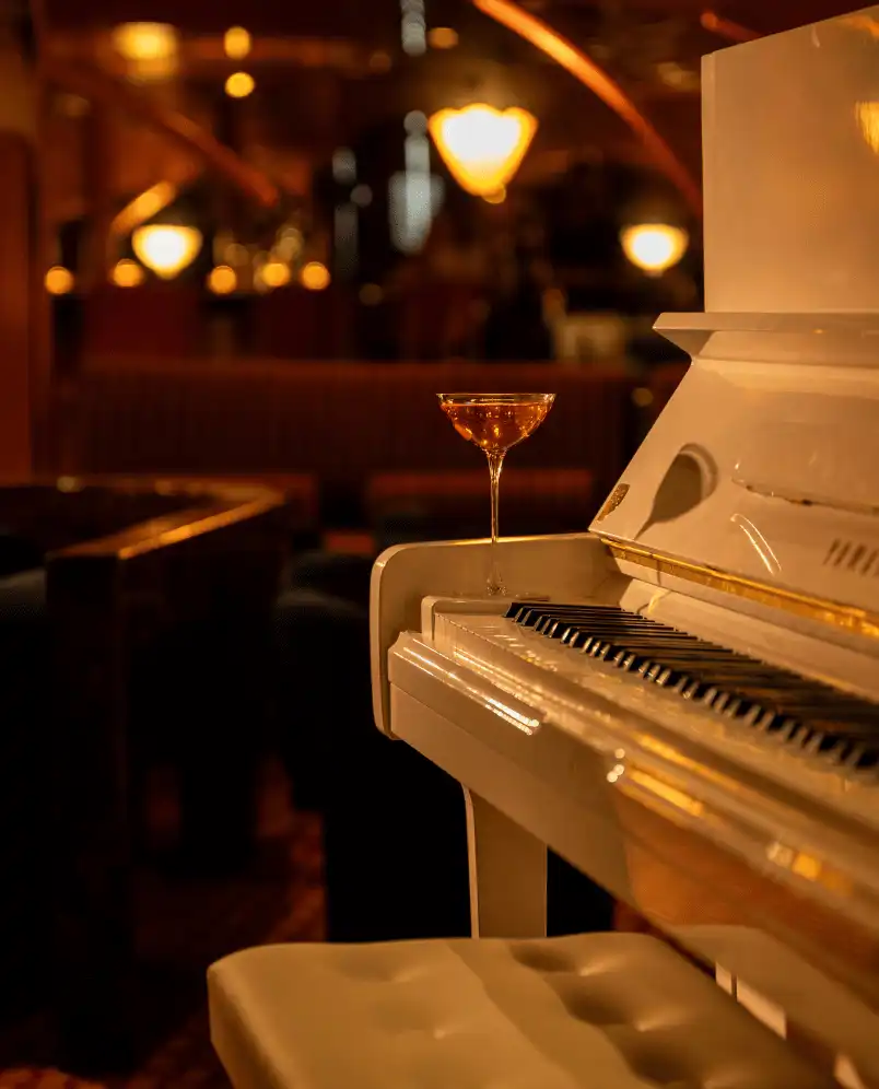 White piano with a cocktail glass on it in a dimly lit lounge with warm lighting.