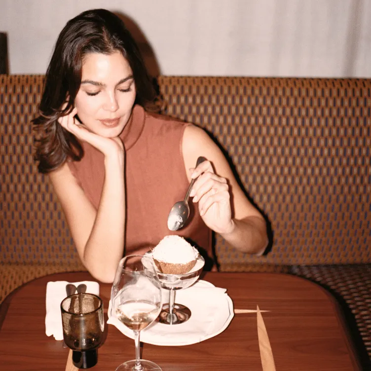 Woman in a sleeveless brown top sitting at a table with a dessert and two glasses of water.