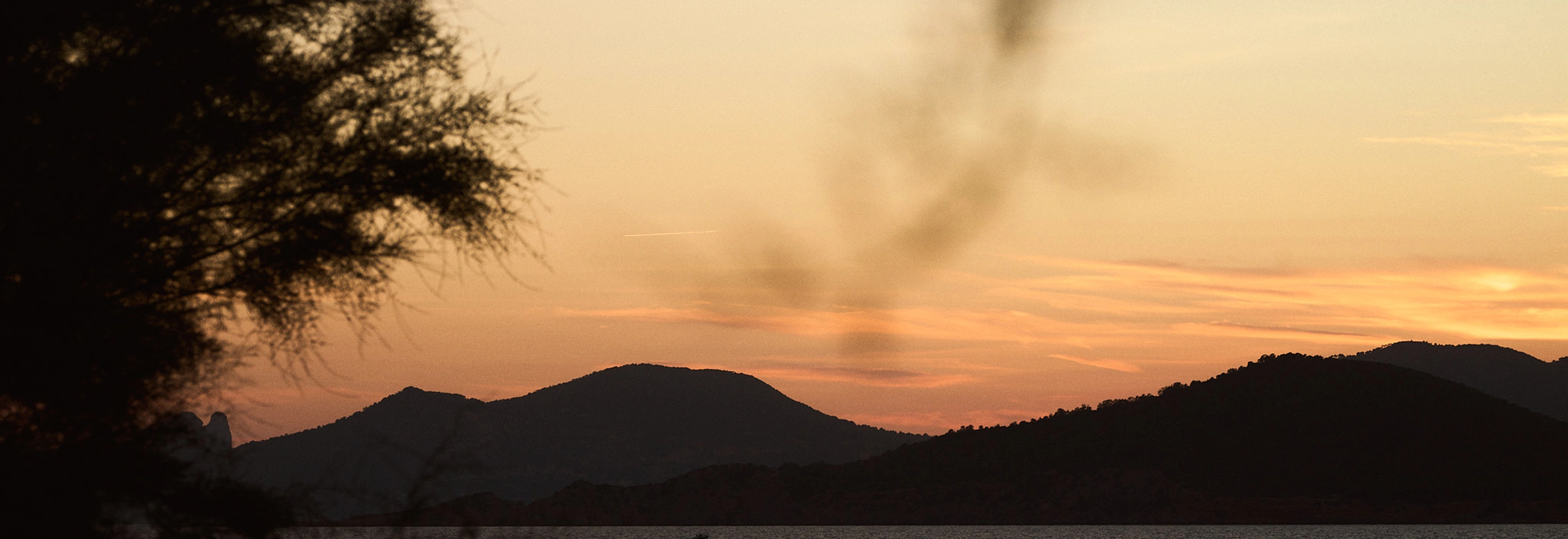 Silhouetted mountains and trees against a pastel orange and pink sunset sky.