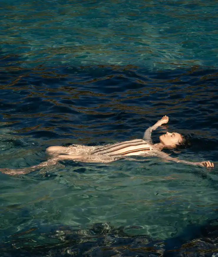 Woman in striped swimsuit floating on her back in clear blue water.