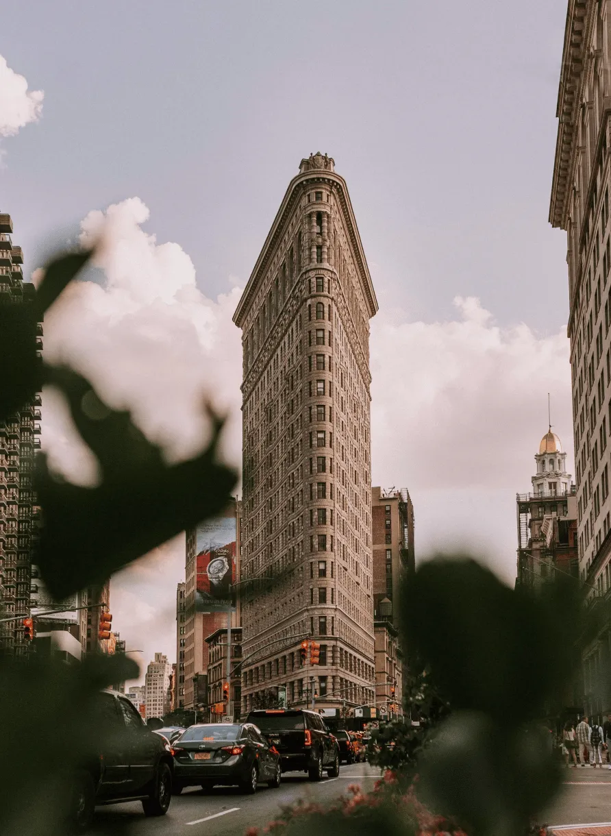 Traffic in front of the iconic Flatiron Building in New York City on a cloudy day.