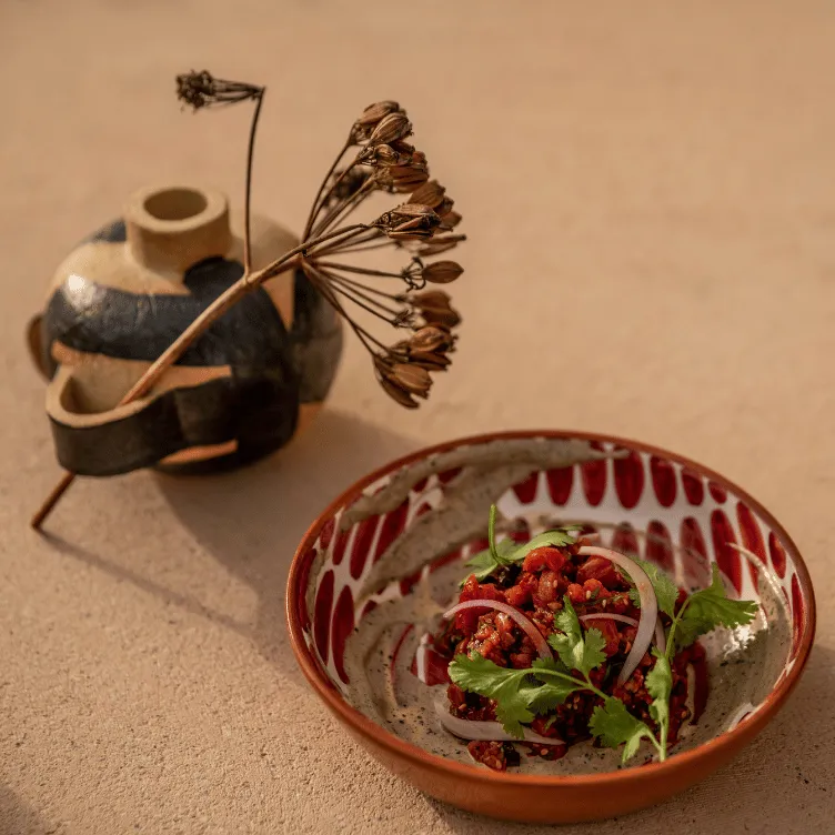 Red bean salad with sliced onions and cilantro in a decorative ceramic bowl next to a black and beige ceramic vase with dried flowers on a beige surface.