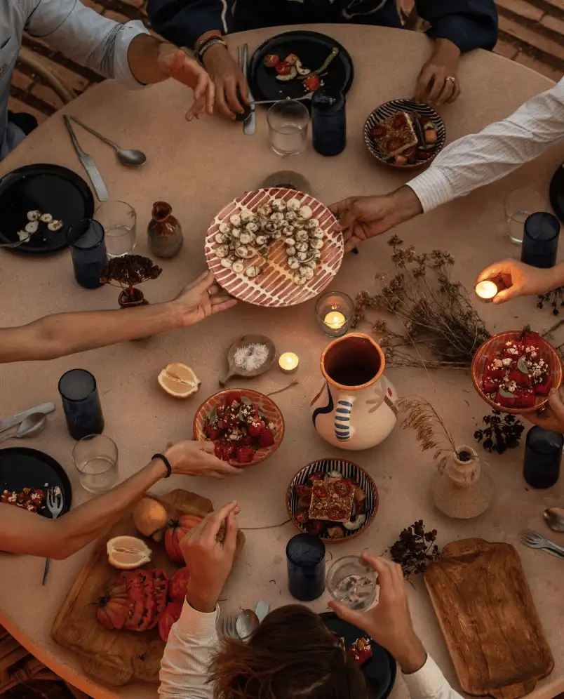 Overhead view of a dining table with people sharing various appetizers, candles, and rustic ceramic dishes.