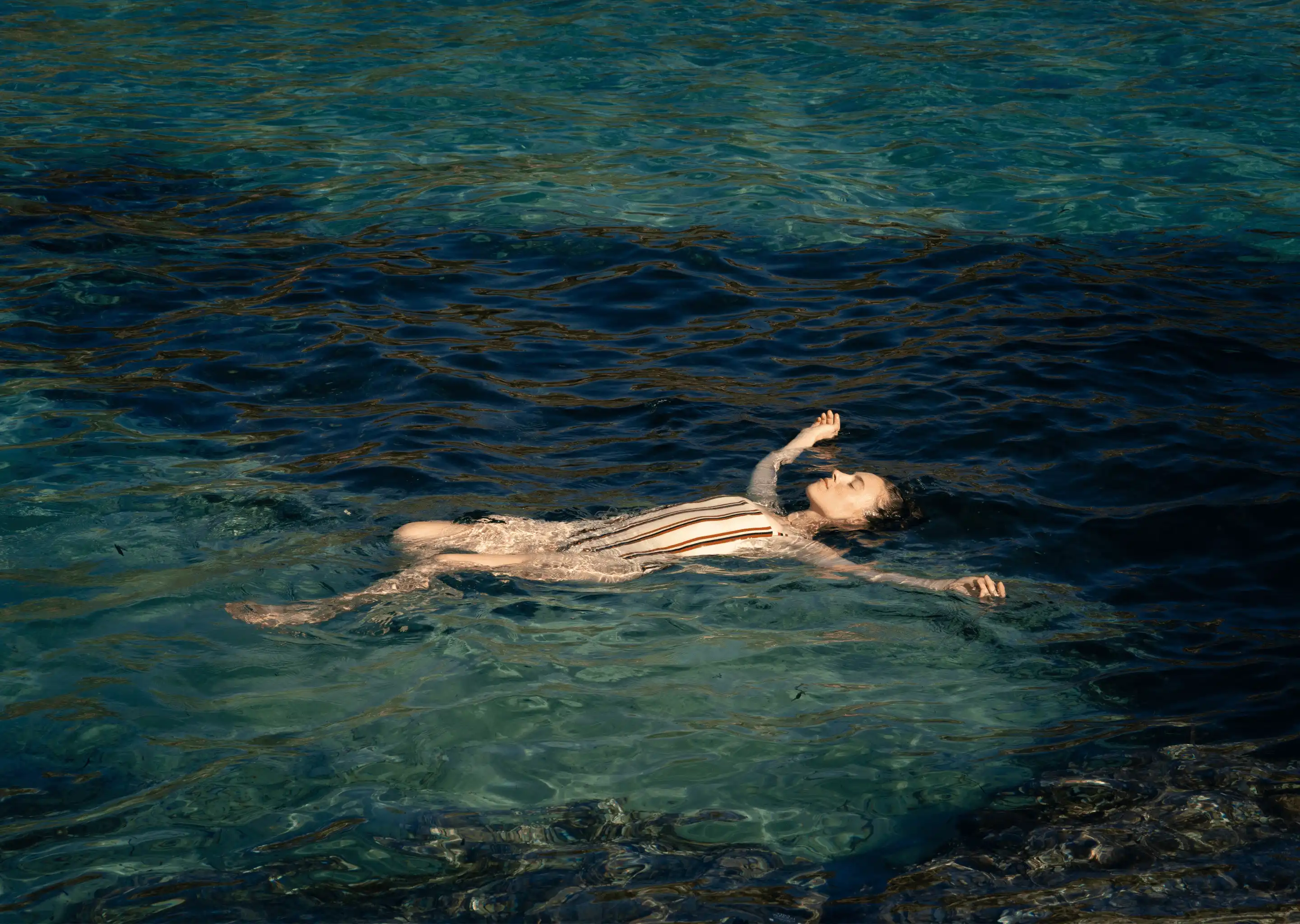 Person floating relaxed on clear blue water with arms and legs spread out.