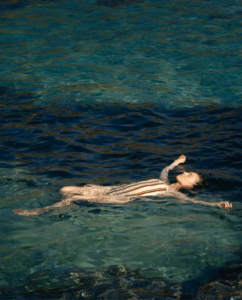 Woman floating relaxed on her back in clear blue-green water.