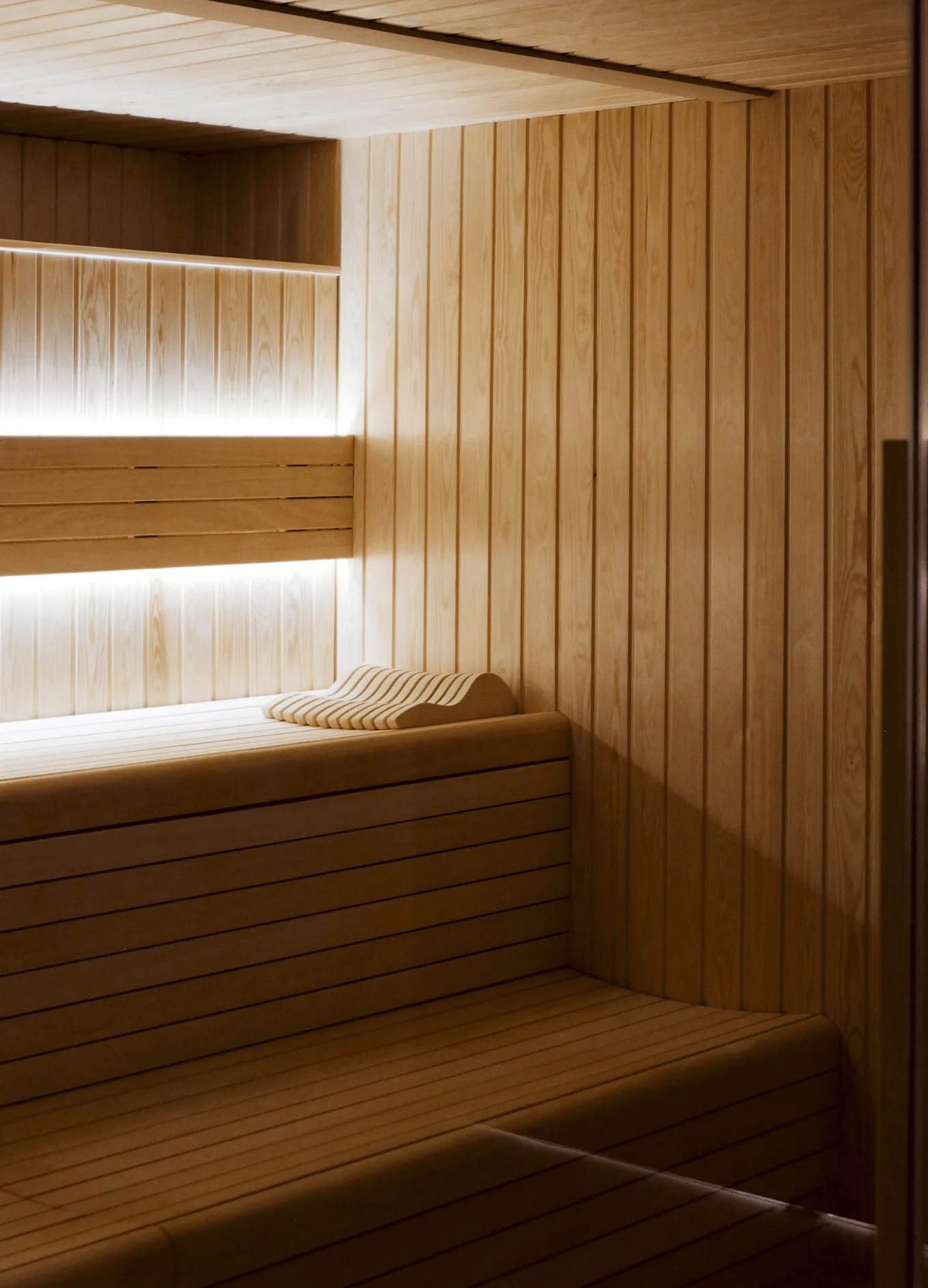 Interior of a wooden sauna with bench seating and a contoured headrest pillow.